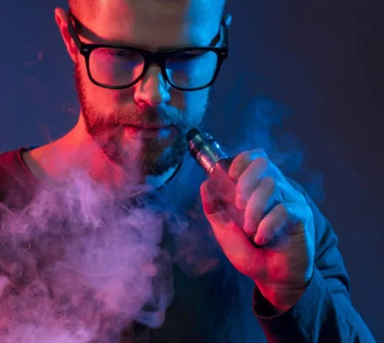 Man with glasses using an electronic cigarette with smoke in a dark setting