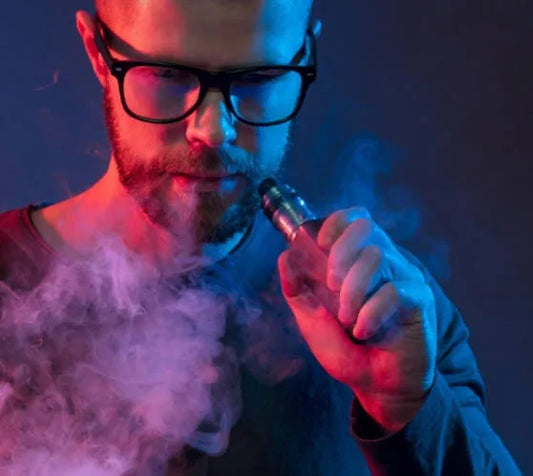 Man with glasses using an electronic cigarette with smoke in a dark setting